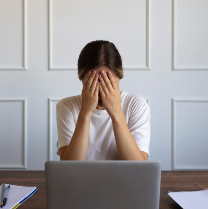A person sitting at a desk with their head in their hands, overwhelmed